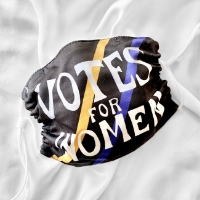 Black cloth mask with white straps. One yellow and one blue diagonal slash each run across the mask behind the white text "Votes for Women"