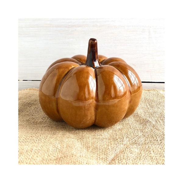 Shiney, brownish, stoneware pumpkin in bright window light resting on burlap. 