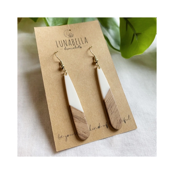 Two-tone, elongated teardrop shape earrings, ivory white on top, wood below. Earrings mounted on brown paper card.