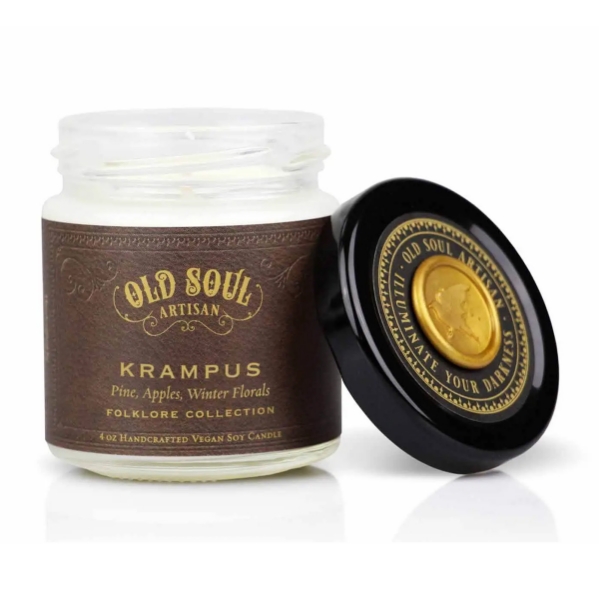 Krampus Candle displayed with cover resting on side. Clear candle jar has a black cover with gold lettering. Brown wrap around candle. 