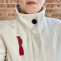 Red brooch in shape of cardinal. Hand carved from natural gourd. Shown pinned on light tan jacket.