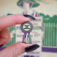 A hand holding the "Votes for Women" Ribbon Enamel Pin