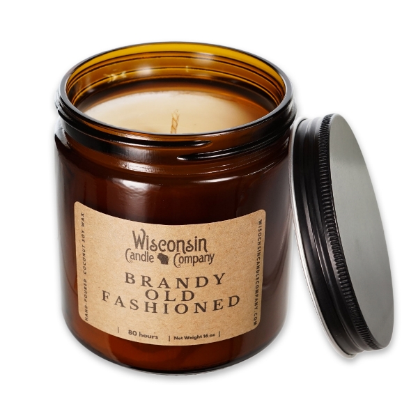 The Brandy Old Fashioned 16 oz candle in brown glass container with black tin screw-on lid. The lid is leaning on the side of the brown glass jar.