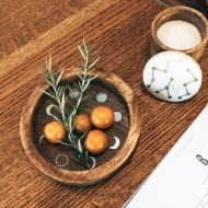 Brown, round, wood dish with metallic moon phase inlays around the perimeter. Shown holding small tomatoes and herb sprigs.