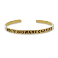 Brass tone Madeline Island Museum souvenir cuff bracelet with the word "Mooniingwanekaaning" stamped in black.