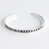 Silver tone Madeline Island Museum souvenir metal cuff bracelet with the word "Mooniingwanekaaning" stamped in black.